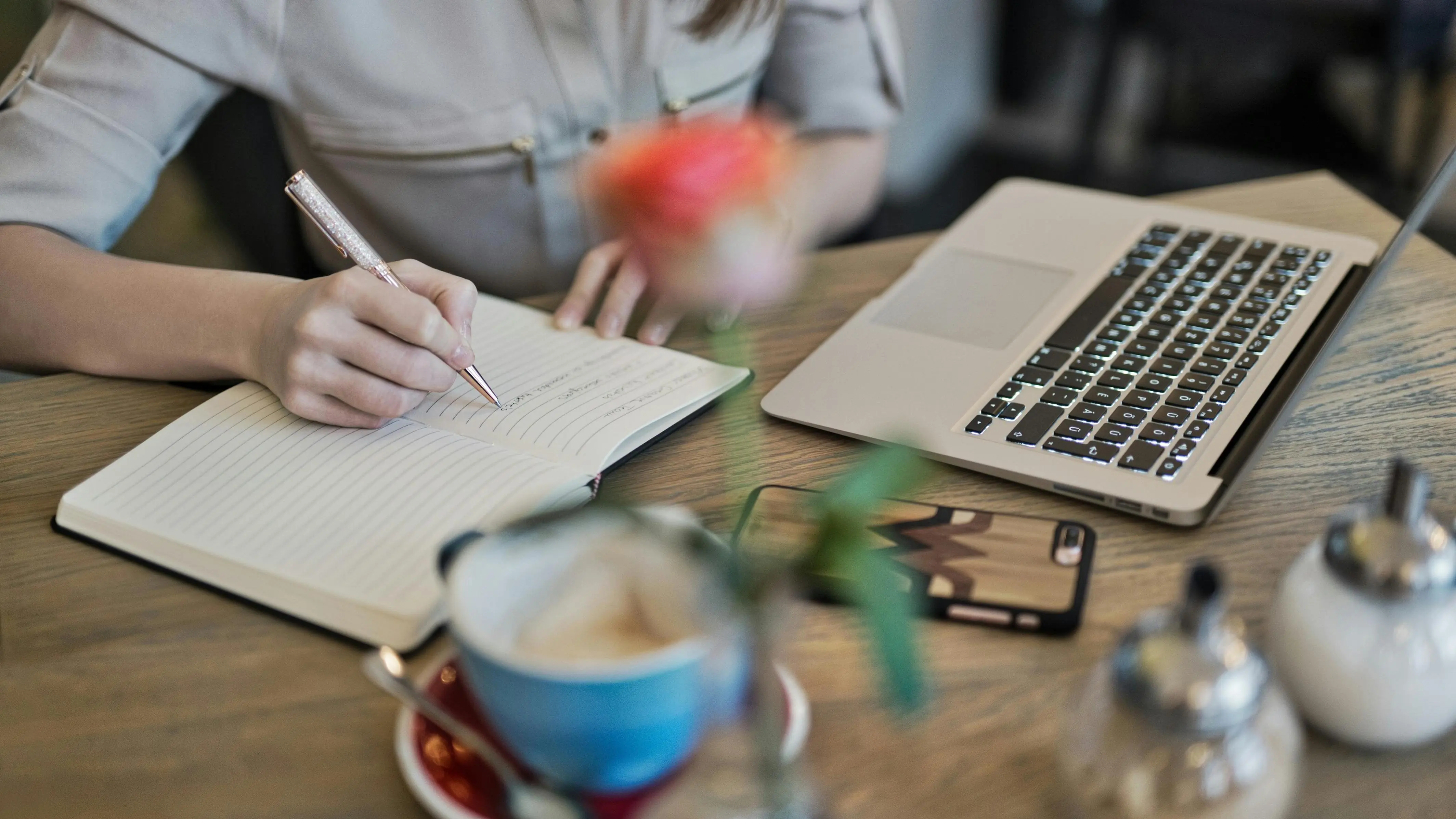 Person writing on a notebook beside MacBook, focused on writing what script readers crave.