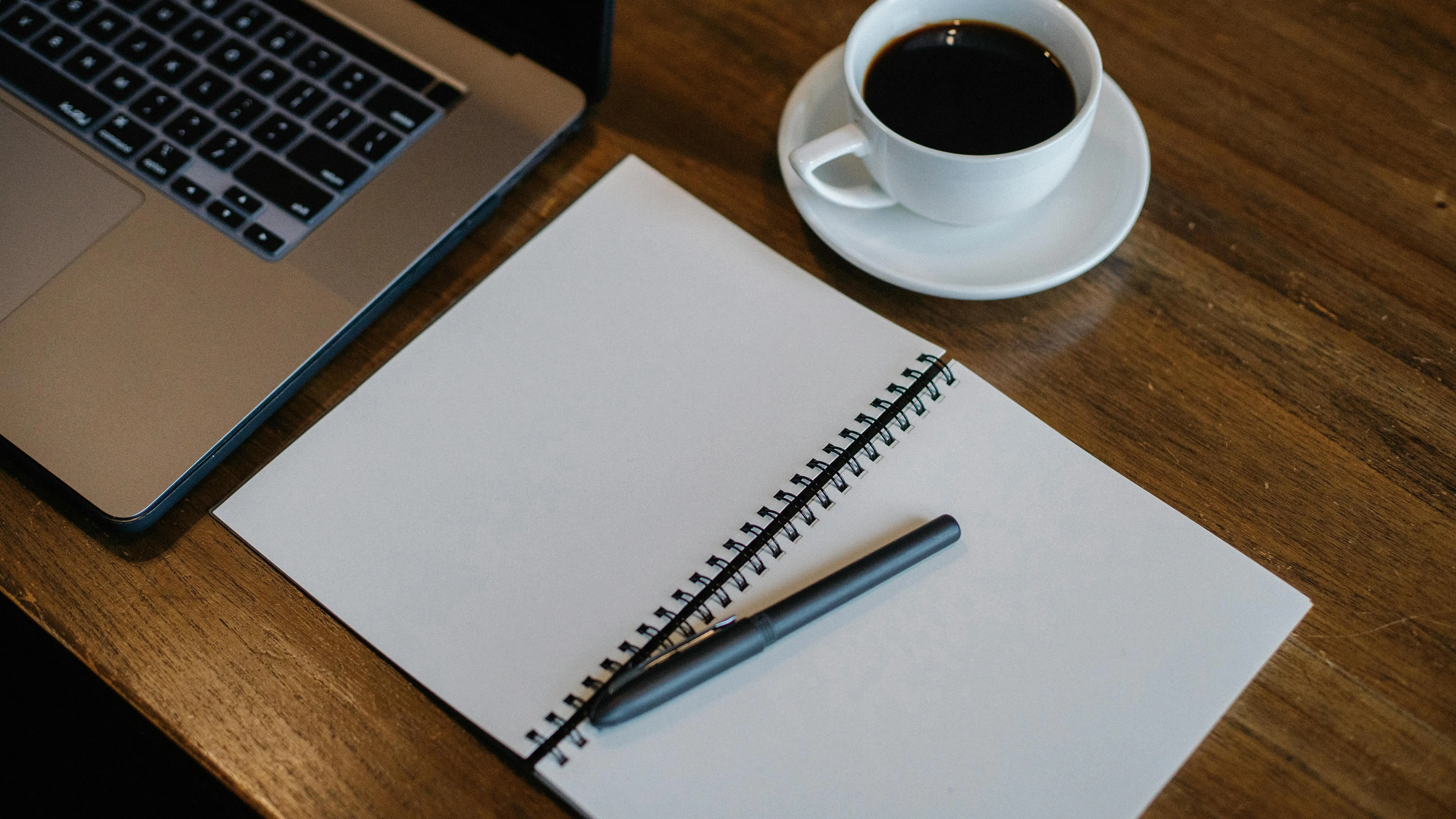 Laptop and notepad with writing schedule near cup of coffee