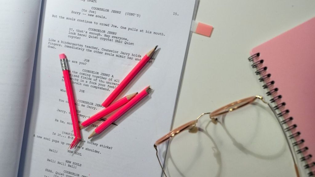 Printed screenplay draft with pink editing pencils and reading glasses, comparing human script reader notes to AI coverage accuracy.