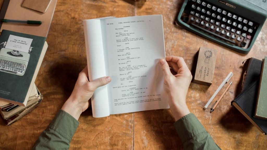 Hands holding a printed screenplay next to a vintage typewriter, contrasting traditional human script notes with AI coverage reports.