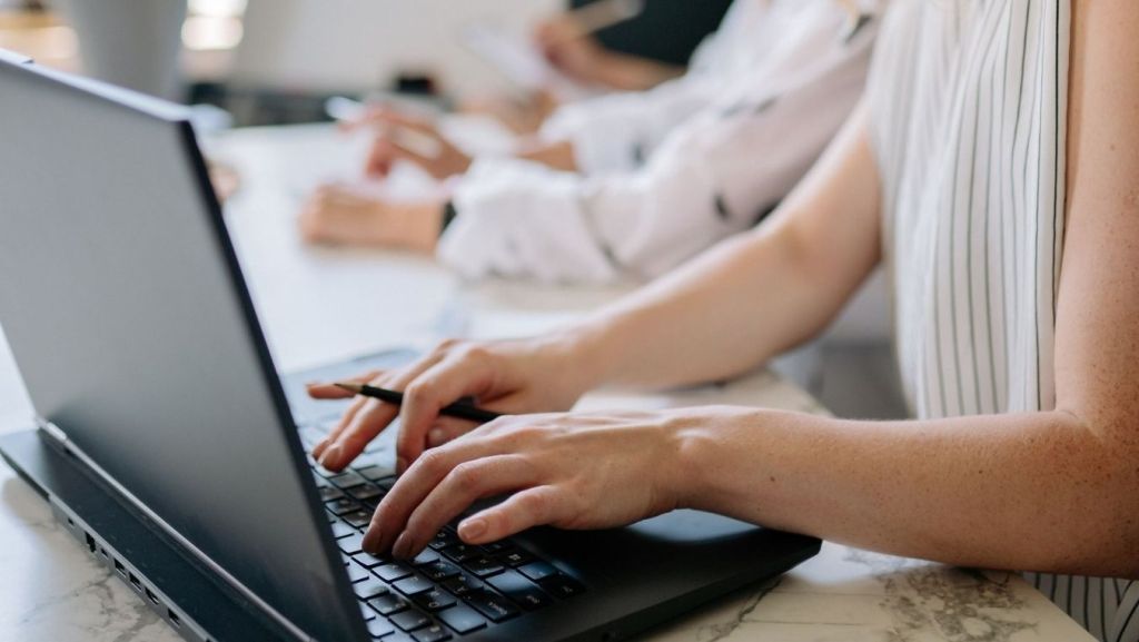 Screenwriter typing on a laptop while holding a pen to integrate AI-assisted tools into a professional scriptwriting workflow.