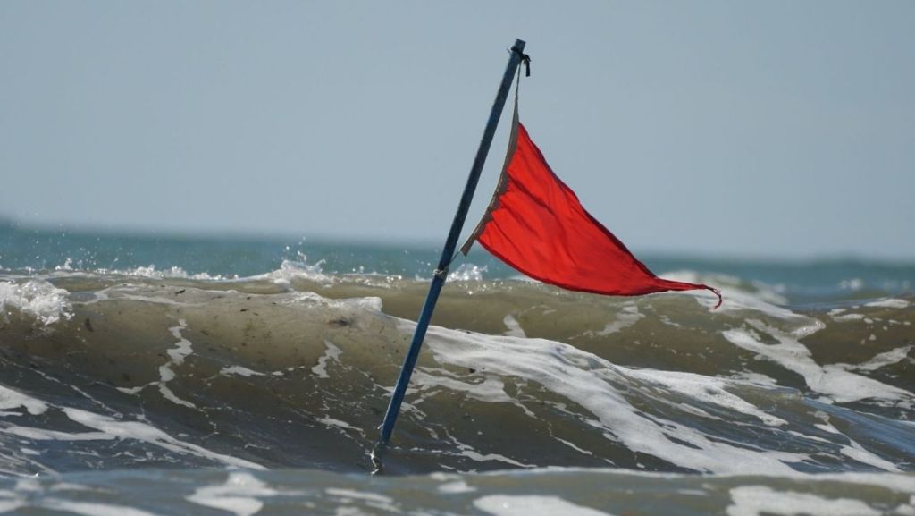 Red warning flag planted in ocean waves symbolizing script coverage reports flagging a weak inciting incident.