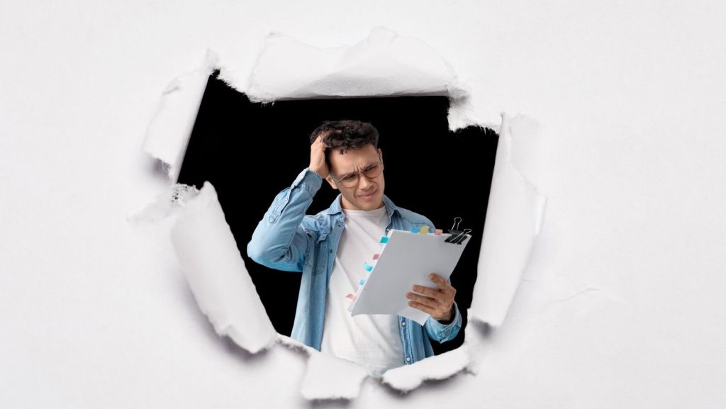 Confused screenwriter reviewing manuscript through a torn paper hole representing AI analysis to spot plot holes in script drafts.