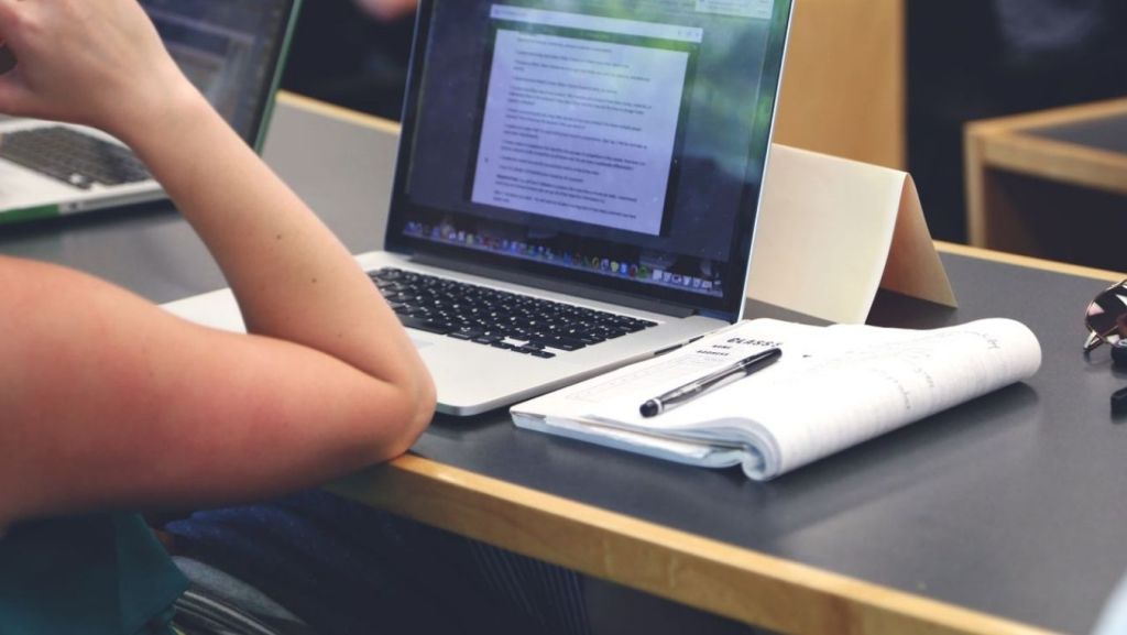 Writer at a desk using a laptop and notepad to apply AI feedback for screenplay coverage and rapid revisions.