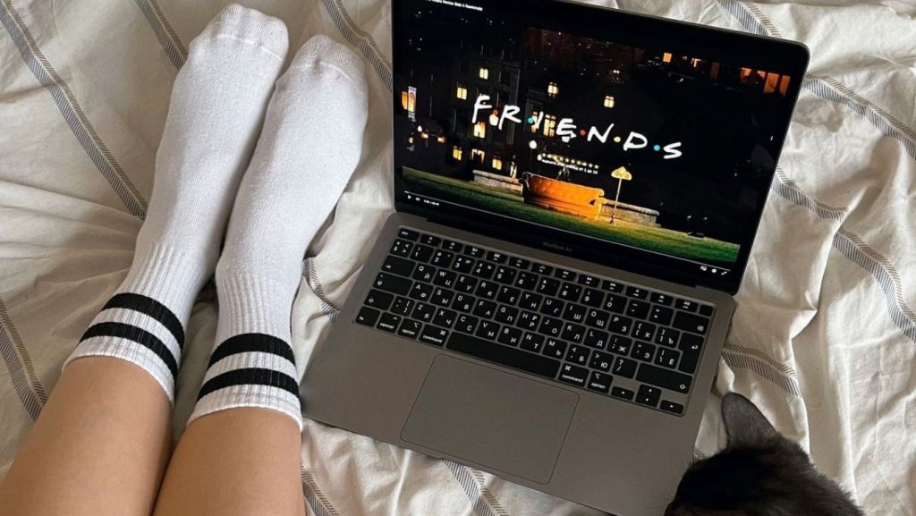 Laptop streaming a TV show pilot in bed, representing AI script coverage and episodic structure analysis.