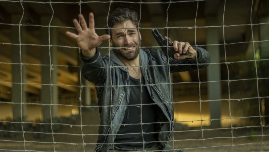 Action hero holding a handgun behind a mesh net, illustrating action screenplay set pieces and pacing analysis.